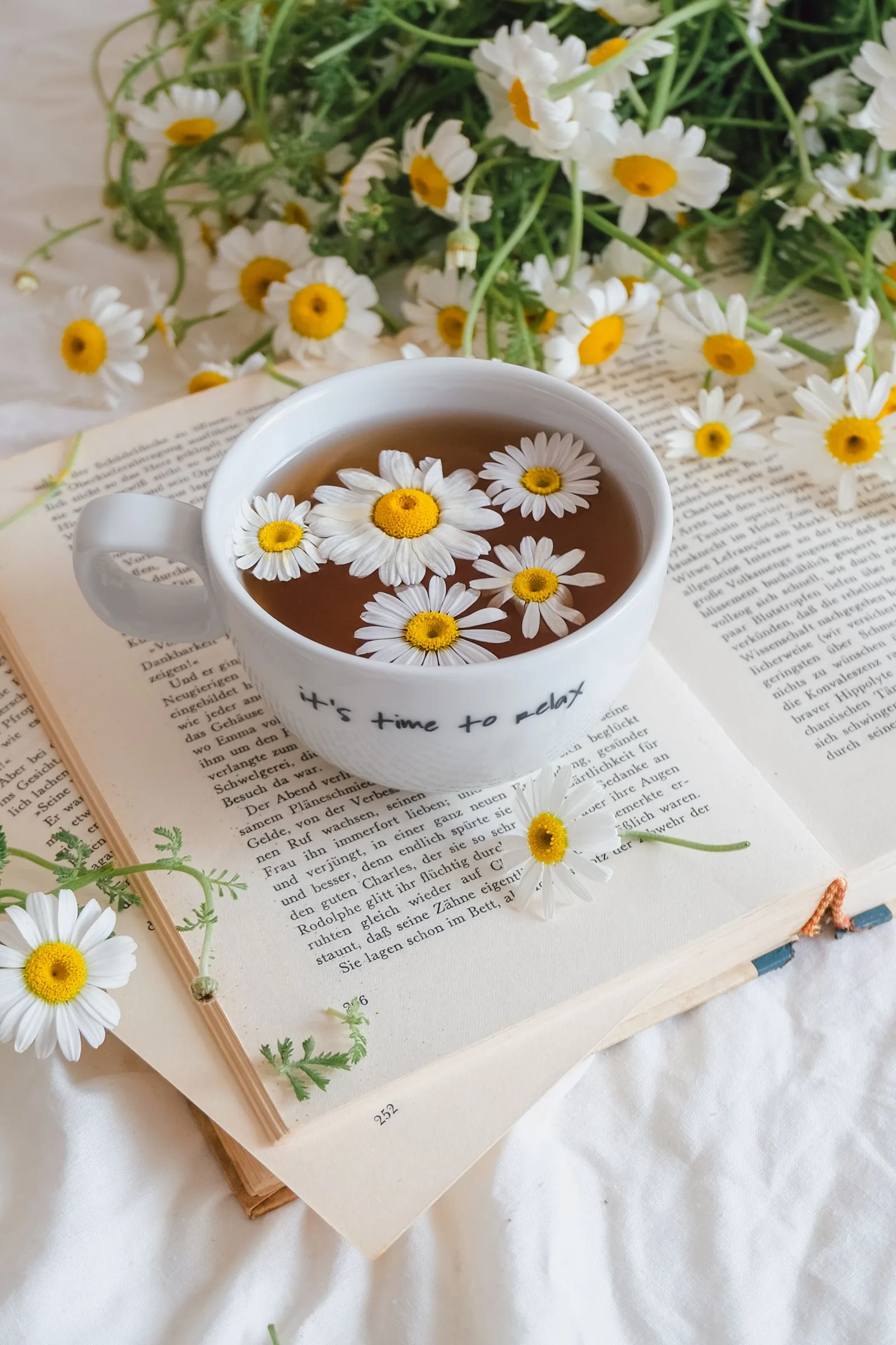 Une tasse de camomille posée sur un livre ouvert, au lit